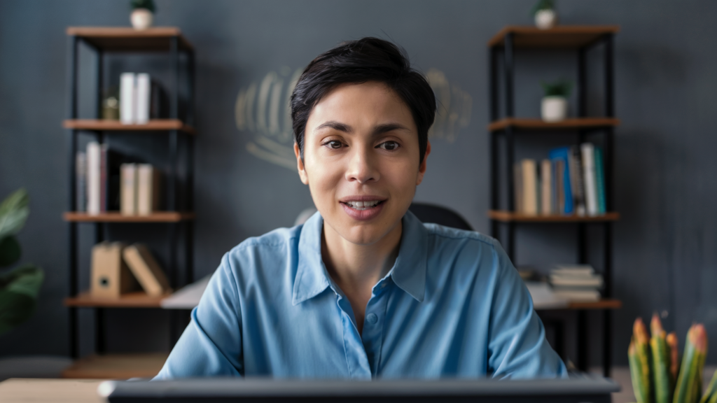 A woman with short dark hair working at a desk with the best desk placement, surrounded by shelves with books and plants in a calm home office setting.