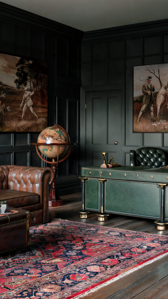 A traditional home office with dark paneled walls, a leather sofa and ottoman, a globe on a stand, a green leather desk with brass accents, and framed hunting scene paintings.