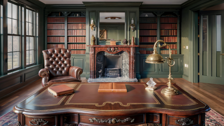 A traditional home office with deep green walls, wooden bookshelves, an ornate wooden desk, and a plush leather armchair by a window, offering a sophisticated and cozy ambiance.